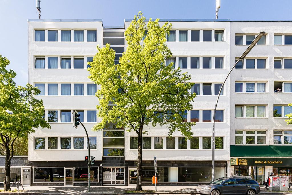 a white building with a tree in front of it at Berlinhome Apartment Steglitz in Berlin