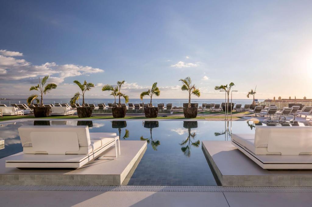 uma piscina com cadeiras e palmeiras e o oceano em Royal Hideaway Corales Suites em Adeje