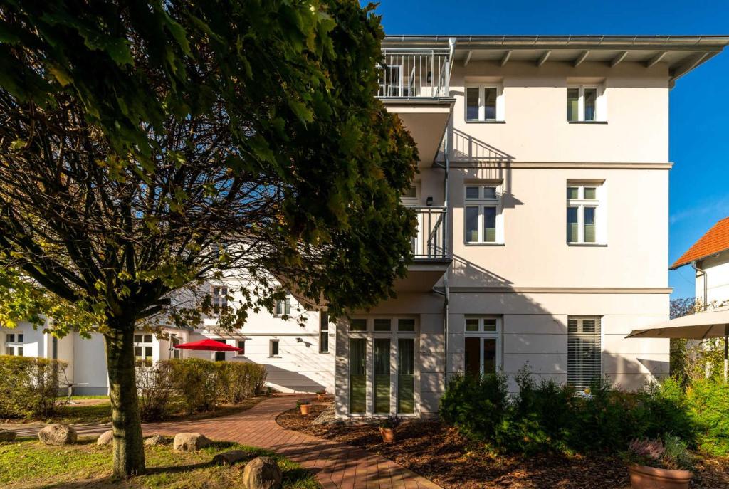 ein weißes Gebäude mit einem Baum davor in der Unterkunft Ferienwohnung "Welle" im Ostsee-Domizil Sandburg in Kühlungsborn