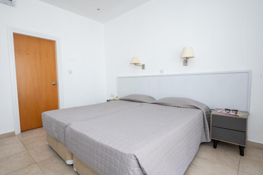 a white bedroom with a bed and a night stand at New Famagusta Hotel & Suites in Ayia Napa