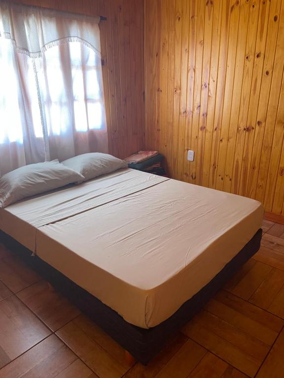 a bed in a room with wooden walls and a window at Cabañas “La India” in Jardín América