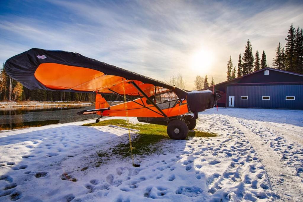 an orange plane sitting on the grass in the snow at Biplane Hangar Lakeviews with Northern Lights in North Pole