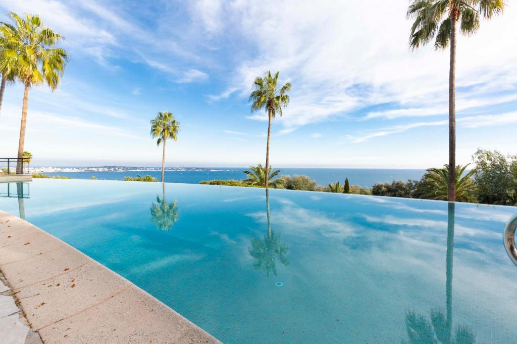une piscine avec des palmiers et l'océan en arrière-plan dans l'établissement Exceptional Super-Cannes Glaïeuls with sea view swimming pools jacuzzi, à Vallauris