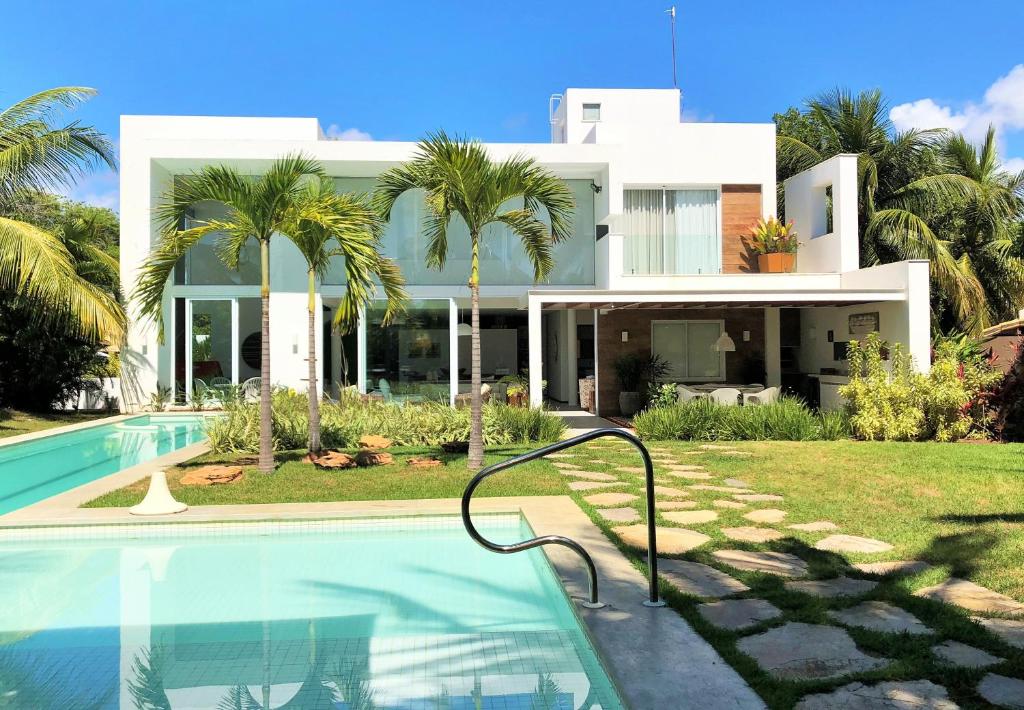 卡馬薩里的住宿－Casa de Praia em Interlagos - 4 suítes a poucos metros do mar，一座大型白色房子,前面设有一个游泳池