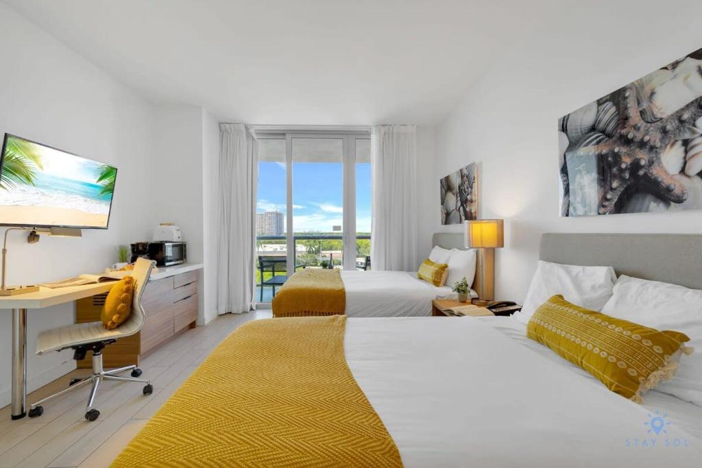 a bedroom with two beds and a desk with a computer at Modern Condo - Amazing Pool - Gym - Balcony in Hallandale Beach