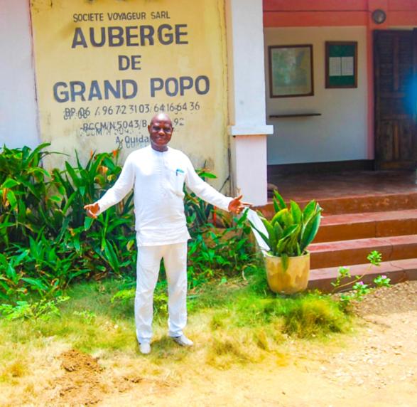 Un uomo in piedi davanti a un palazzo con le braccia aperte di Auberge de Grand Popo a Grand-Popo