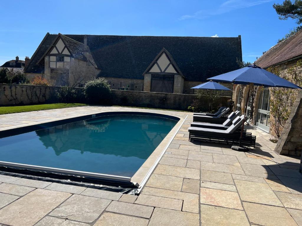 a swimming pool with two lounge chairs and an umbrella at Two Luxury Cosy Cottages in Tewkesbury