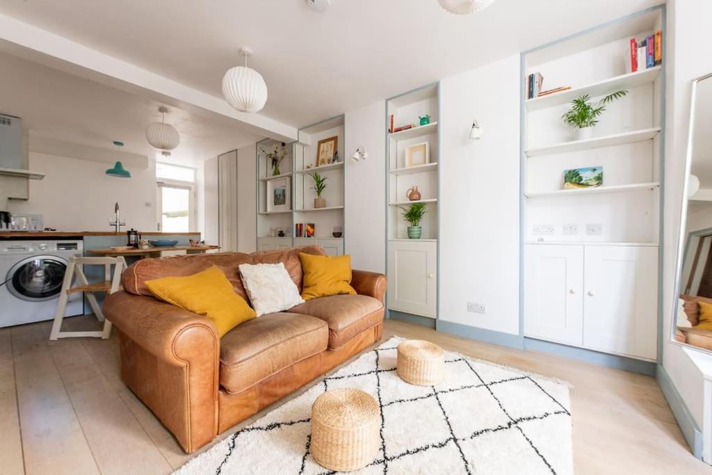 a living room with a brown couch and a kitchen at Lovely self-contained basement studio with kitchen in London