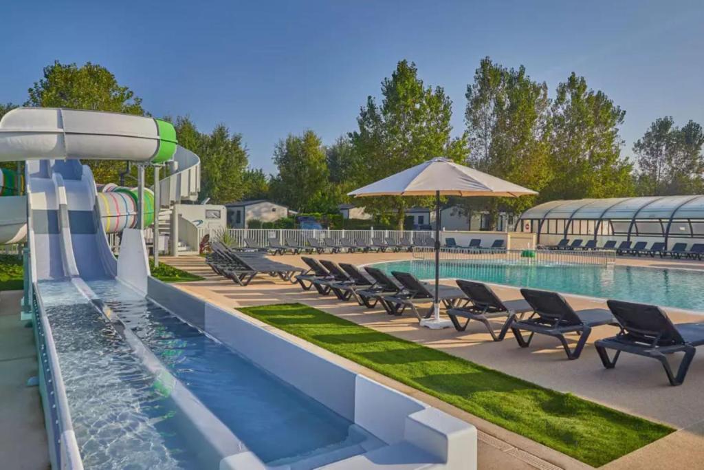 a pool at a resort with chairs and an umbrella at Mobil Home 3 chambres in Ouistreham
