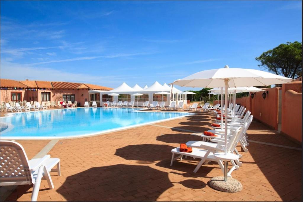 una piscina con sedie bianche e ombrelloni di Résidence Pierre & Vacances Vignola Mare a Vignola Mare