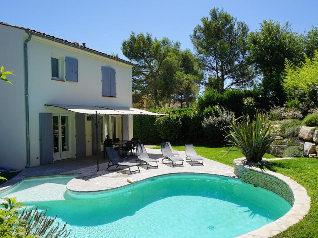 a swimming pool with chairs and an umbrella next to a house at Golf de Pont Royal Villa du Lac climatisée 3 chambres Piscine chauffée Parking et Garage in Mallemort