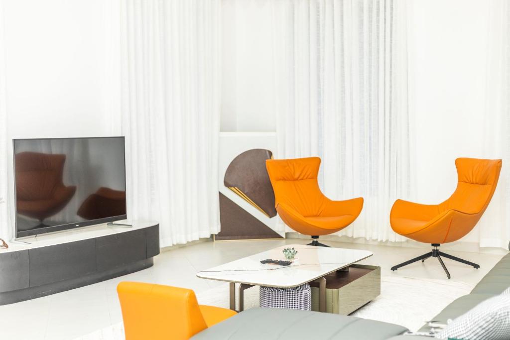 sala de estar con sillas de color naranja y TV en BWAGAmoyo by Enamour en Yombo