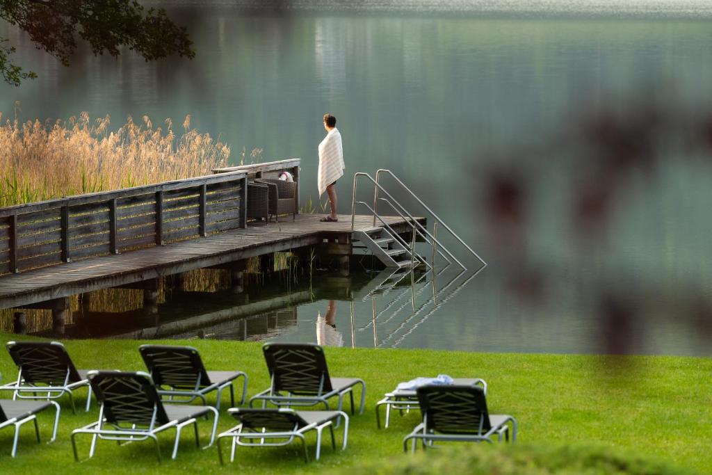 a man standing on a dock next to chairs at Seehotel Urban in Bodensdorf