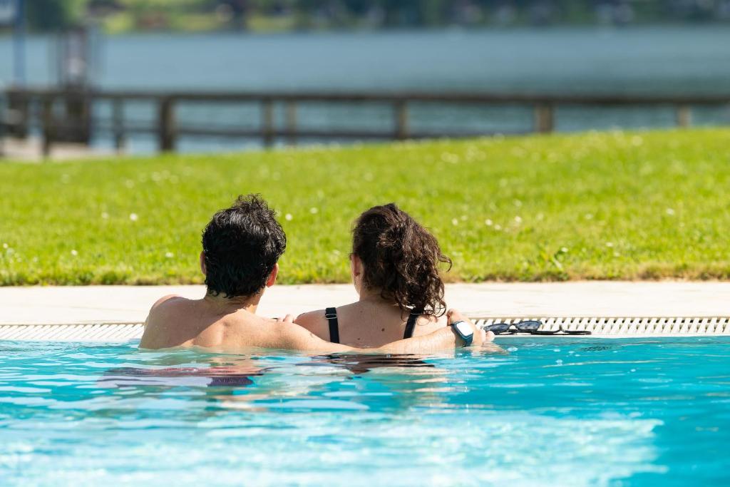 a man and woman sitting in a swimming pool at Seehotel Urban in Bodensdorf