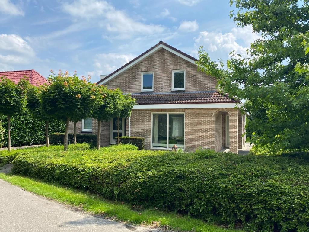 a brick house with bushes in front of a street at Big Family villa 12p big garden with bathtub and jacuzzi in Zeewolde