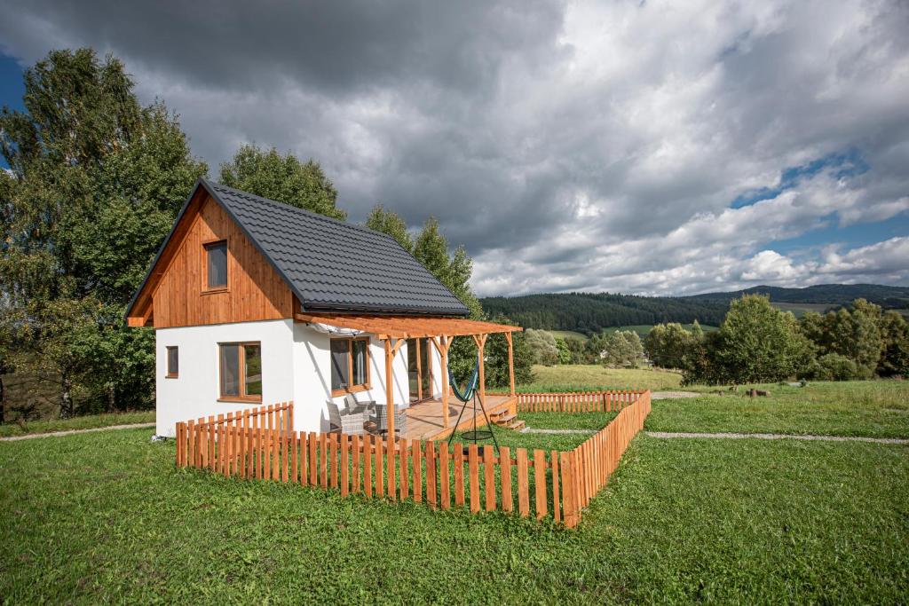 ein kleines Haus mit einem Holzzaun auf einem Feld in der Unterkunft Pastelova Krova - domki w Bieszczadach in Ustrzyki Dolne