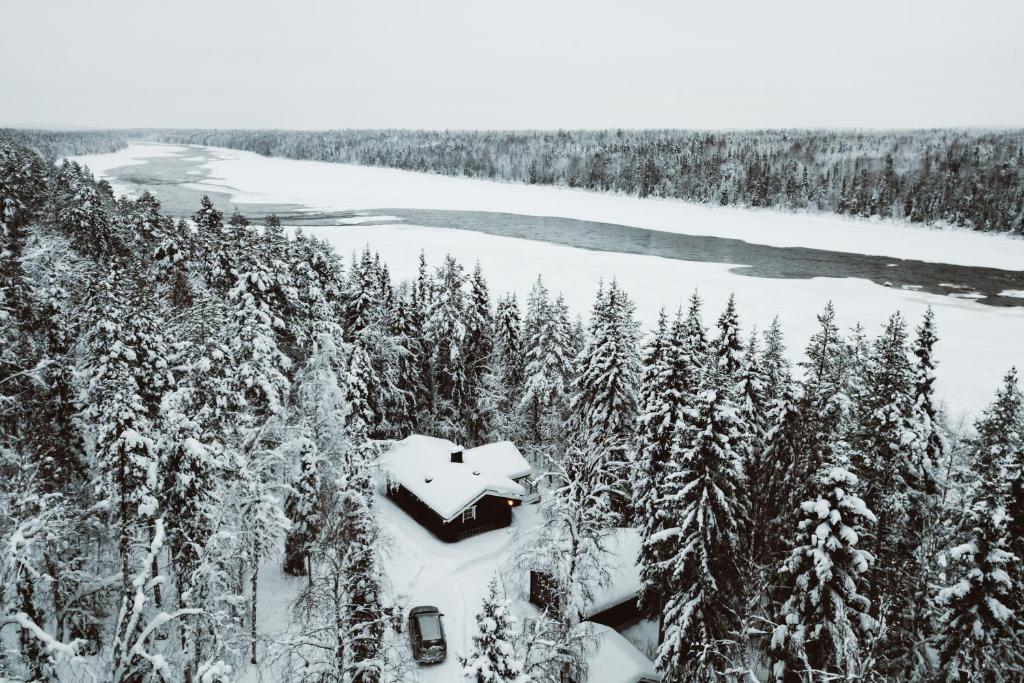 a cabin in the snow next to a river and trees at Villa Lappee in Kolari