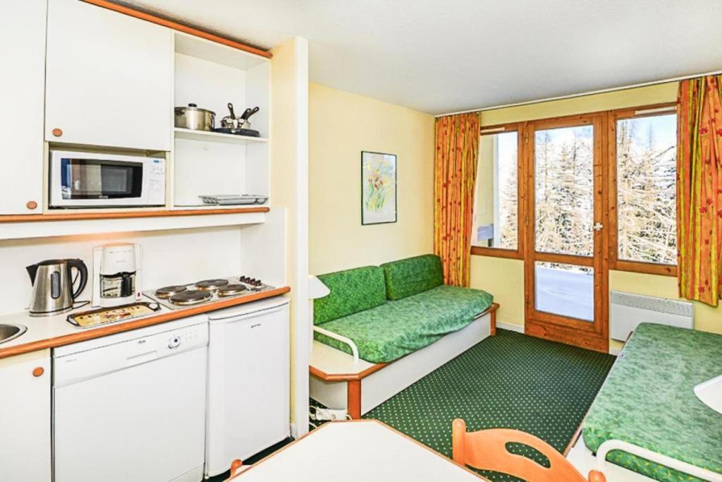 Cette chambre comprend une petite cuisine avec un canapé vert. dans l'établissement Résidence Le Hameau du Sauget - maeva Home - Studio 4 Personnes Budget MAE-1981, à La Plagne Tarentaise