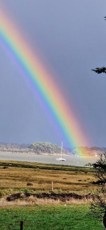 un arc-en-ciel sur un champ avec un bateau dans l'eau dans l'établissement LE COTTAGE, à Séné