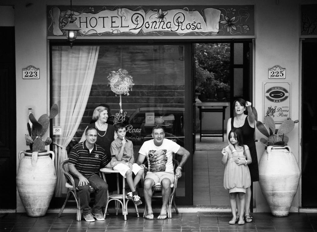 uma foto a preto e branco de uma família sentada em frente a uma loja em Hotel Donna Rosa em SantʼAlessio Siculo