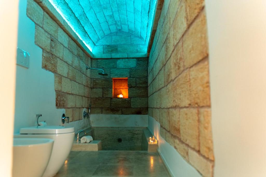 e bagno con parete in pietra, servizi igienici e vasca. di Azalea Suite Deluxe a Sannicola