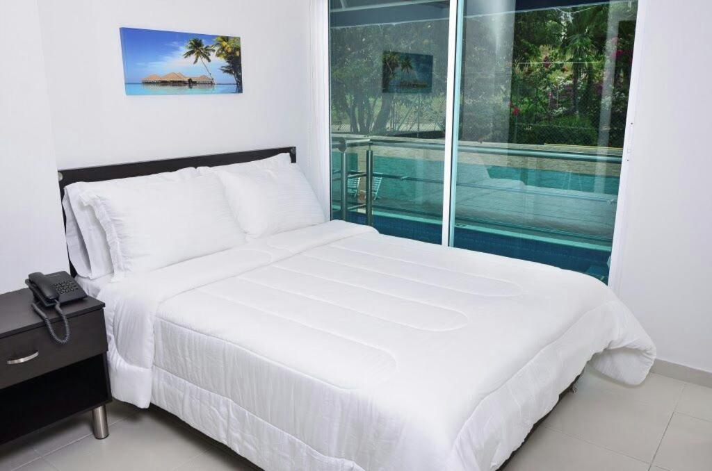 Cama blanca en habitación con ventana grande en HOTEL AQUARELLA DEL MAR, en Santa Marta