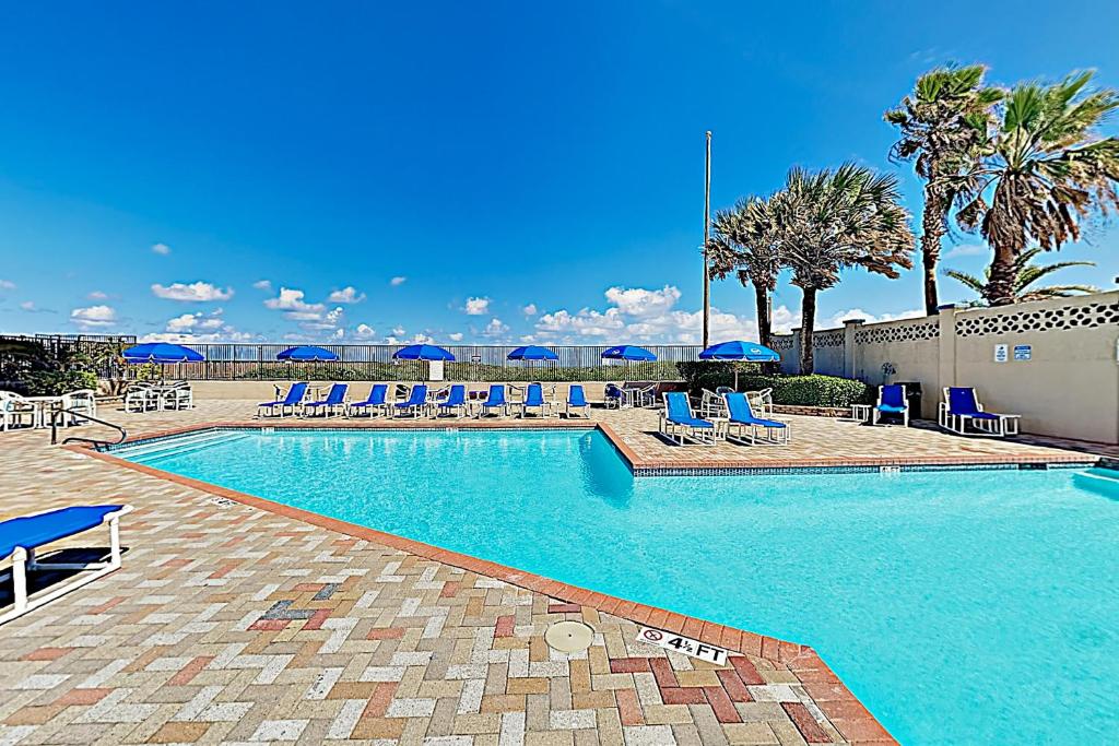 a swimming pool with blue chairs and umbrellas at Suntide III Condominiums in South Padre Island