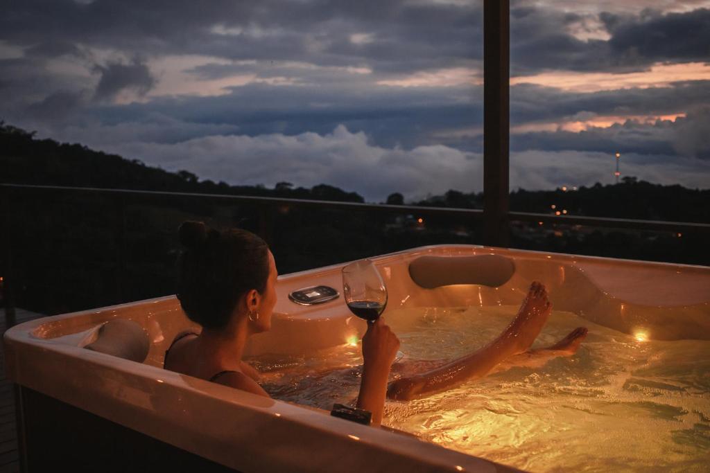Ananta Forest - Glamping Dome - Hot Tub - Sunset & Gulf View في مونتيفيردي كوستاريكا: امرأة في حوض الاستحمام مع كوب من النبيذ
