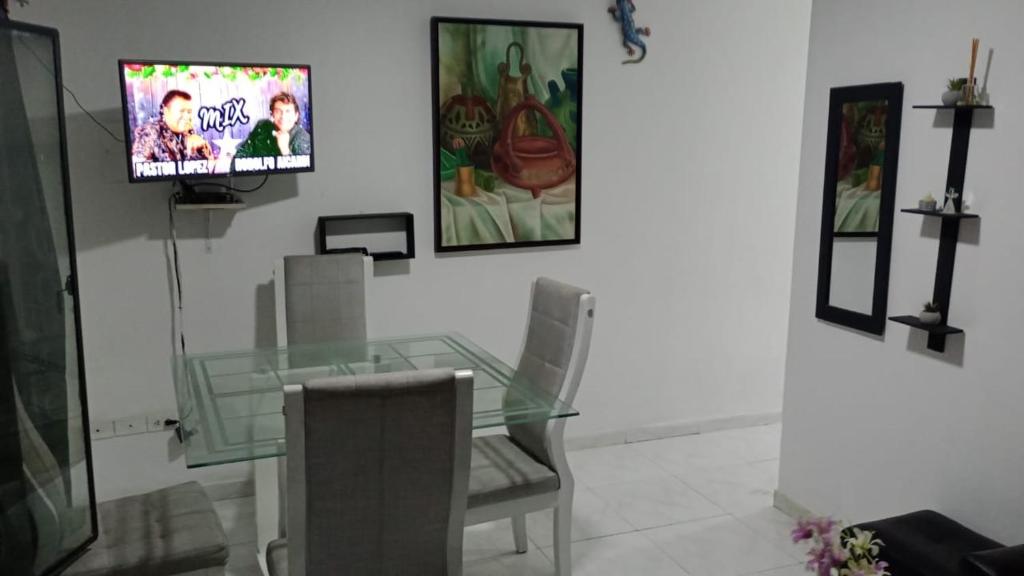 a glass table and chairs with a television on a wall at Casa con calor de hogar con aire acondicionado in Neiva