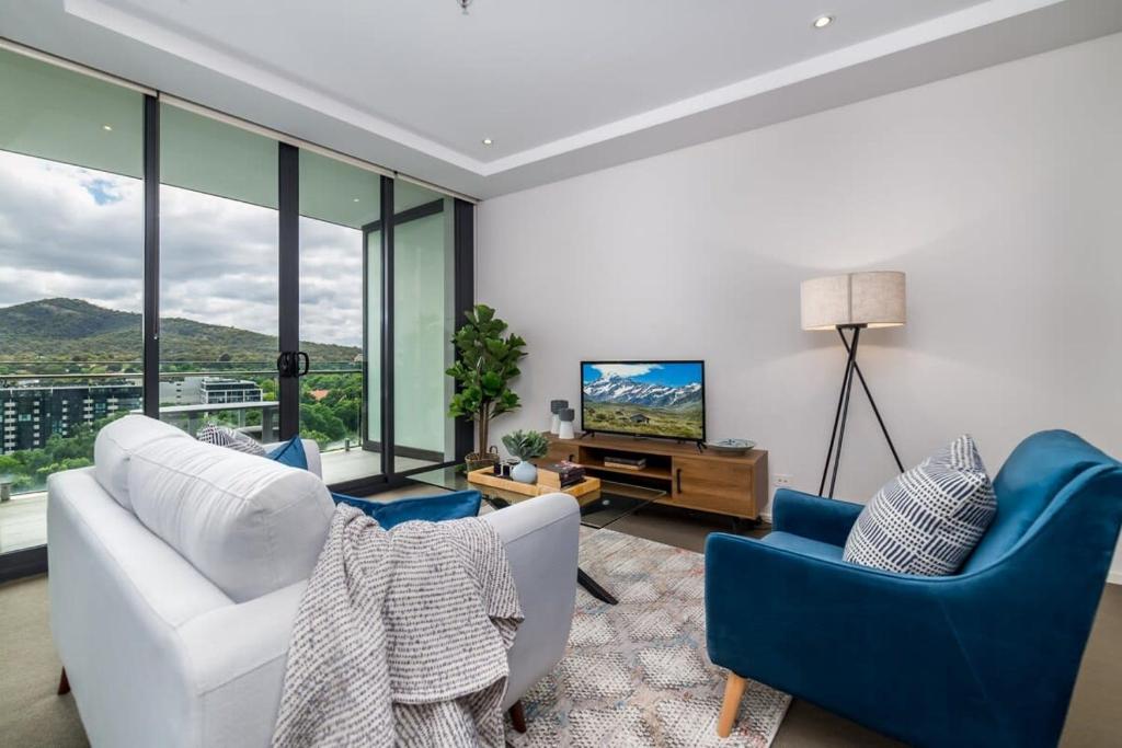 a living room with blue chairs and a television at Executive Balcony Apartment in Central Canberra in Canberra