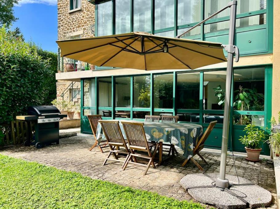une table et des chaises avec un parasol en face d'un bâtiment dans l'établissement Bucolique Rez-de-jardin, 4 pers, proche Disney, à Thorigny-sur-Marne