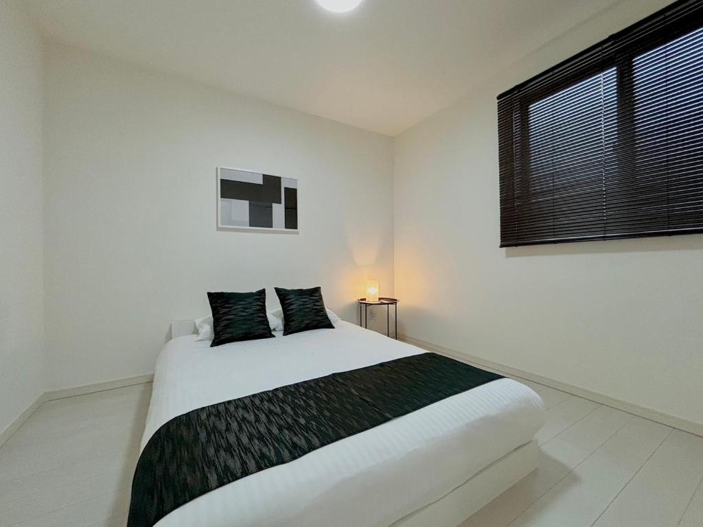 a white bedroom with a large bed and a window at Neighbor's Hotel 楽々園 in Hiroshima