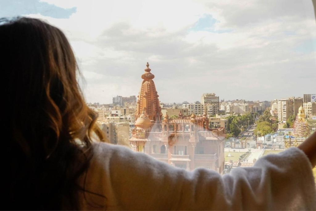 uma mulher a olhar pela janela para uma cidade em Baron Hotel Cairo no Cairo