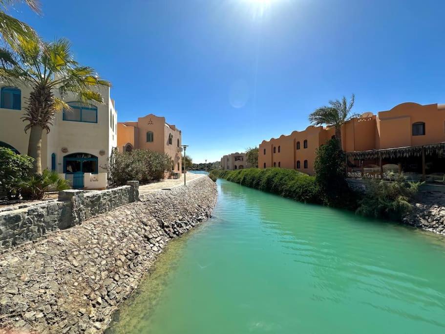 a river with buildings and palm trees next to a street at Central & Unique 1 BR Apt/ in Downtown @ElGouna in Hurghada