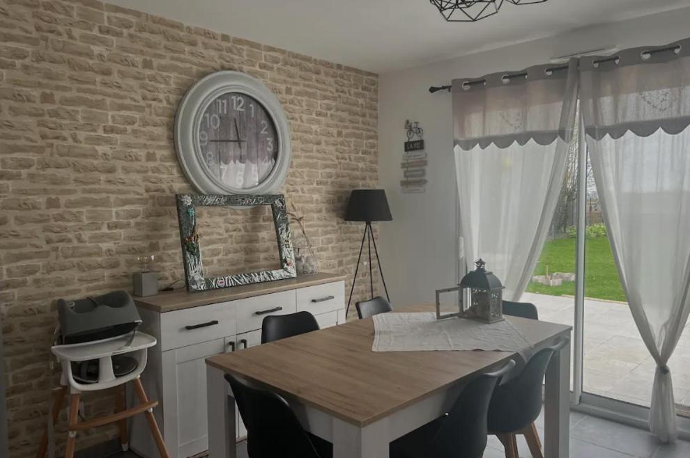 une salle à manger avec une table et une horloge sur un mur de briques dans l'établissement Petite maison au calme, à Poupry