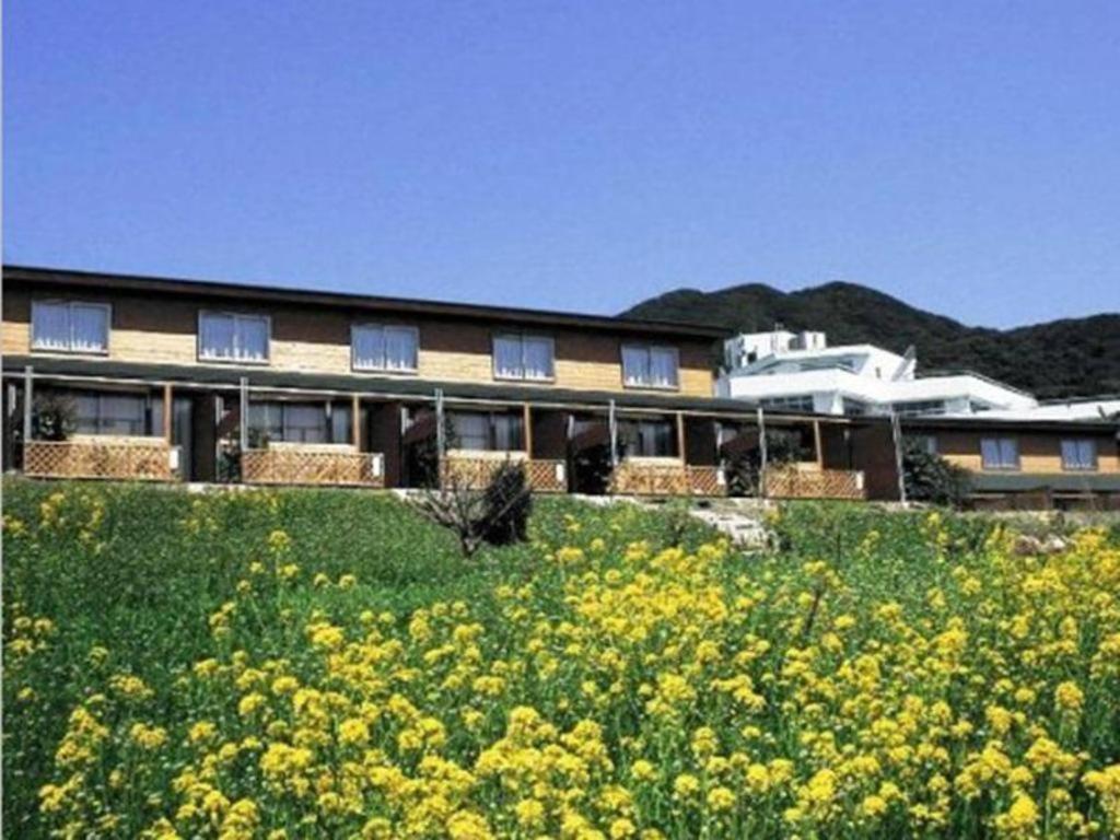 a building on a hill with a field of yellow flowers at Ashizuri Onsen Ashizuri Sunnyside Hotel in Isa