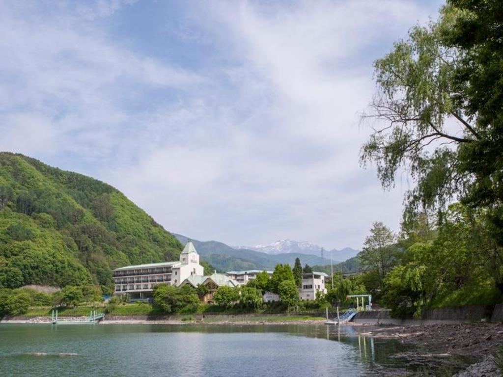 un edificio a orillas de un lago con montañas en el fondo en Takato Sakura Hotel en Ina
