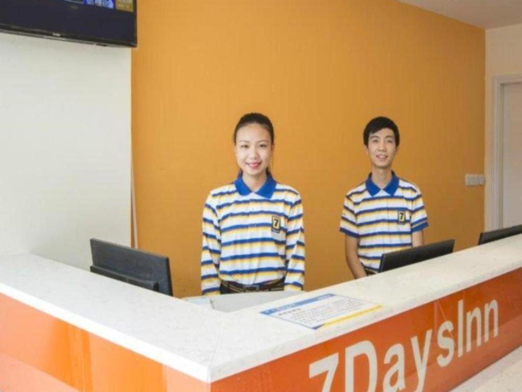 zwei junge Männer stehen hinter einem Schreibtisch in einem Büro in der Unterkunft 7 Days Inn Ya'an Langqiao Pedestrian Street Center in Ya'an