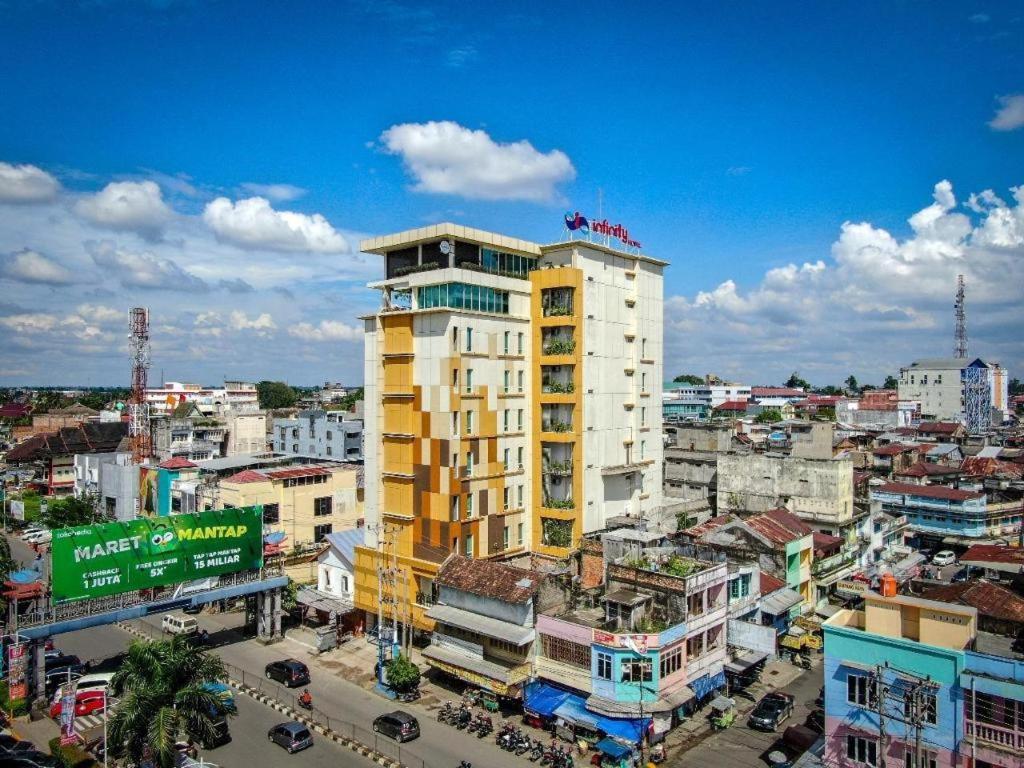 a tall yellow building in a city with buildings at Infinity Hotel Jambi by Tritama Hospitality in Jambi