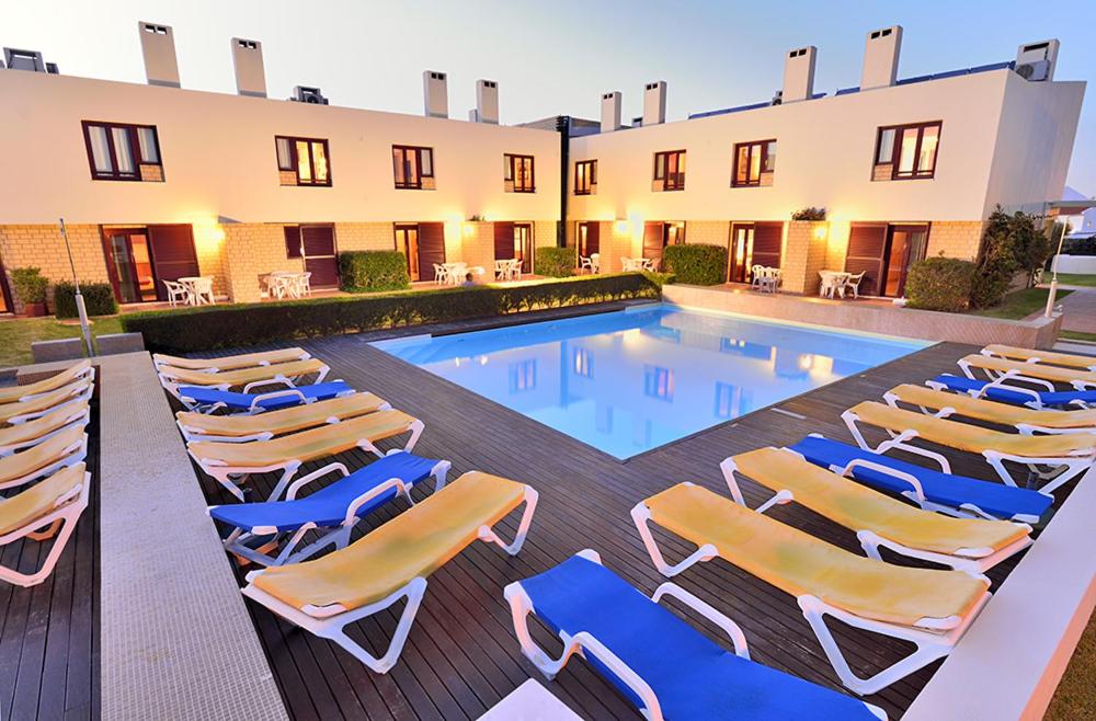 a group of lounge chairs and a swimming pool at Hotel Apartamento Porto Covo in Porto Covo