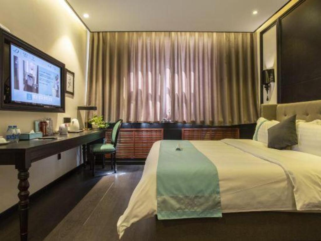 a hotel room with a bed and a desk and a television at Xana Hotelle Shihezi Junken Museum Branch in Shihezi