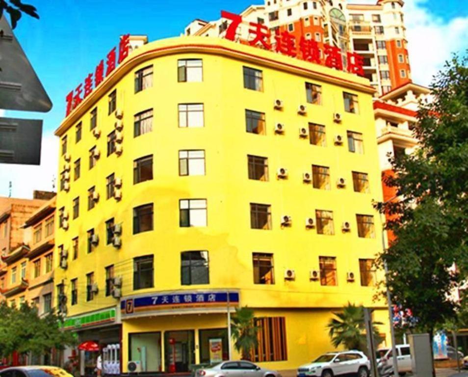 7 Days Inn Xingyi Wanfenglin Xiawutun في Xiawutun: مبنى اصفر فيه سيارات تقف امامه