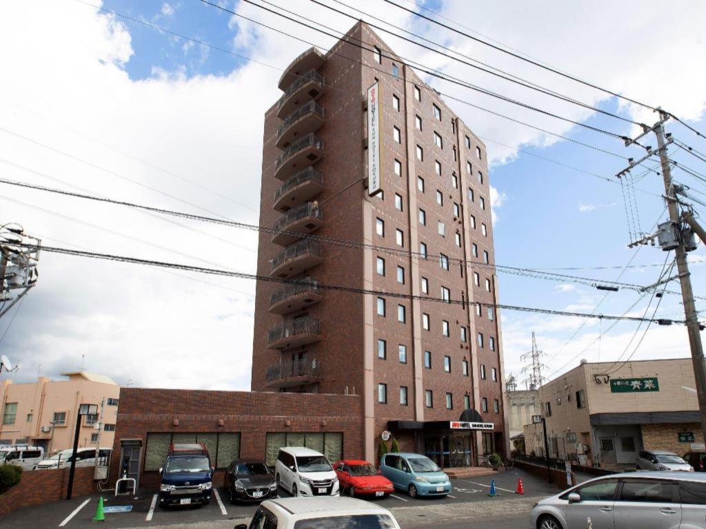 un edificio alto de ladrillo con coches estacionados en un estacionamiento en OYO Sun Hotel Kokubu Kagoshima en Kirishima