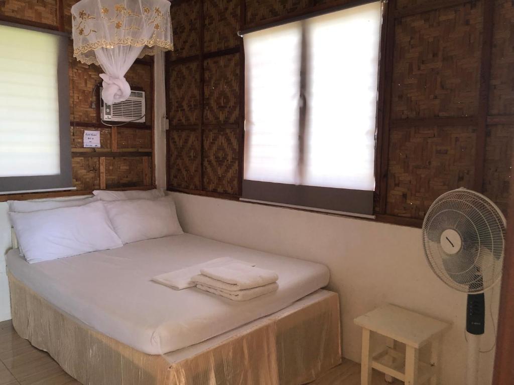 Cama en habitación con ventilador y 2 ventanas en MIOKI HOMETEL en Batuan