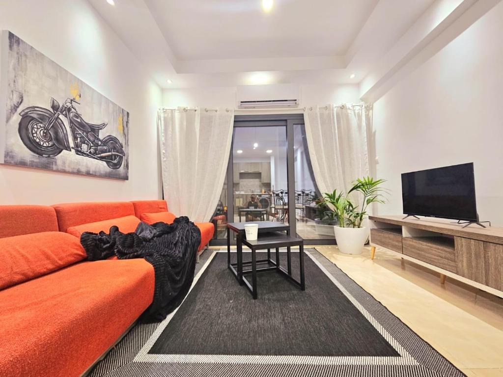ein Wohnzimmer mit einem orangenen Sofa und einem Flachbild-TV in der Unterkunft 1BD Beach Apartment in Paphos City