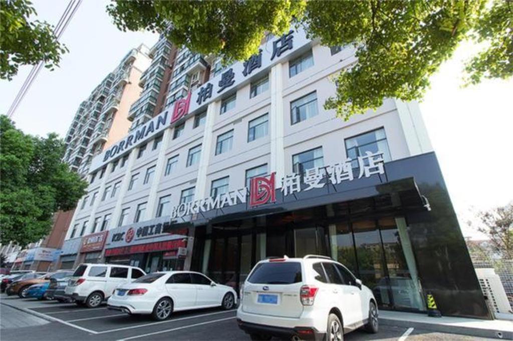 Borrman Hotel Jingzhou Jiangjin West Road Wanda Plaza Fantawild في Caoshi: مبنى ابيض كبير به سيارات تقف في موقف للسيارات