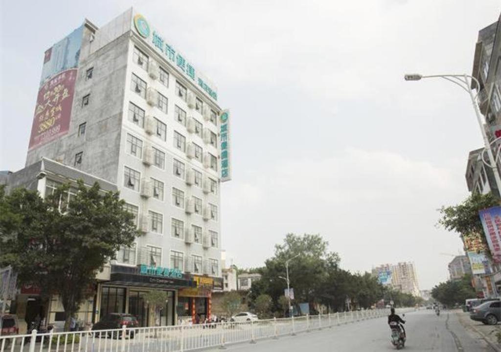 a building on a city street with a person riding a motorcycle at City Comfort Inn Luchuan Hot Spring Plaza High-speed Railway Station 
