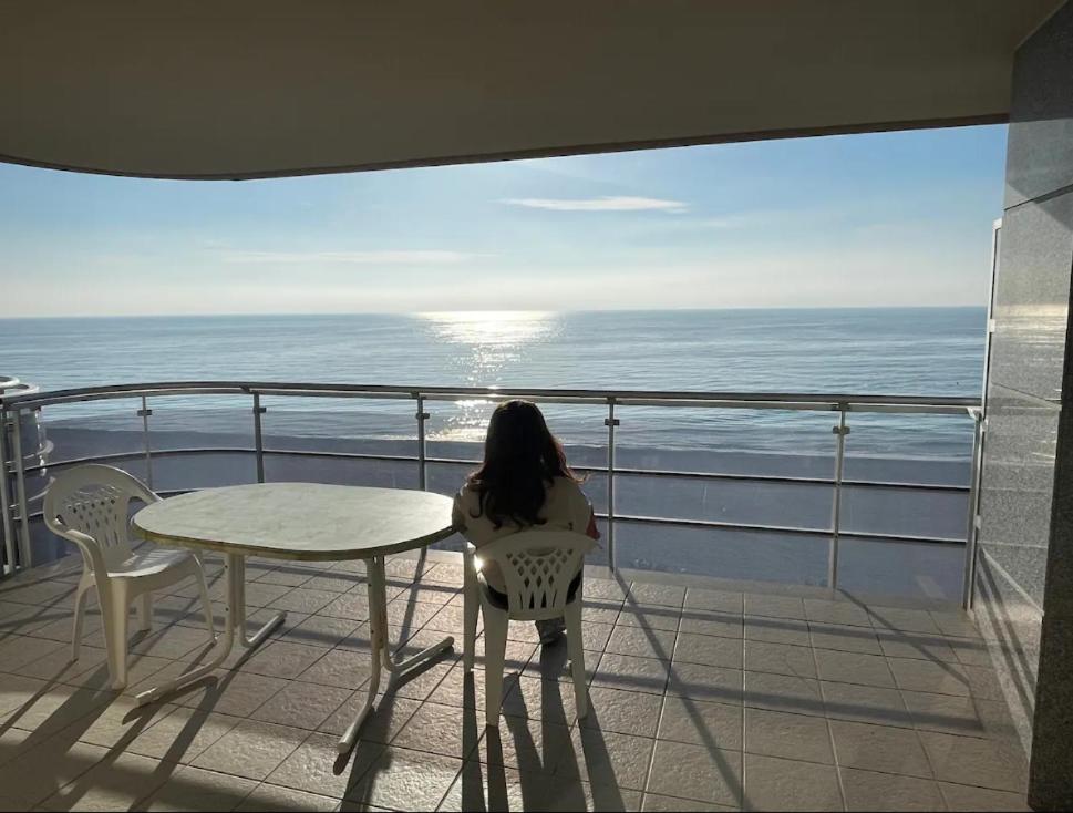 une femme assise à une table sur un balcon donnant sur l'océan dans l'établissement Apartamentos-Atico Reformados Pompeya I y II, à Peñíscola