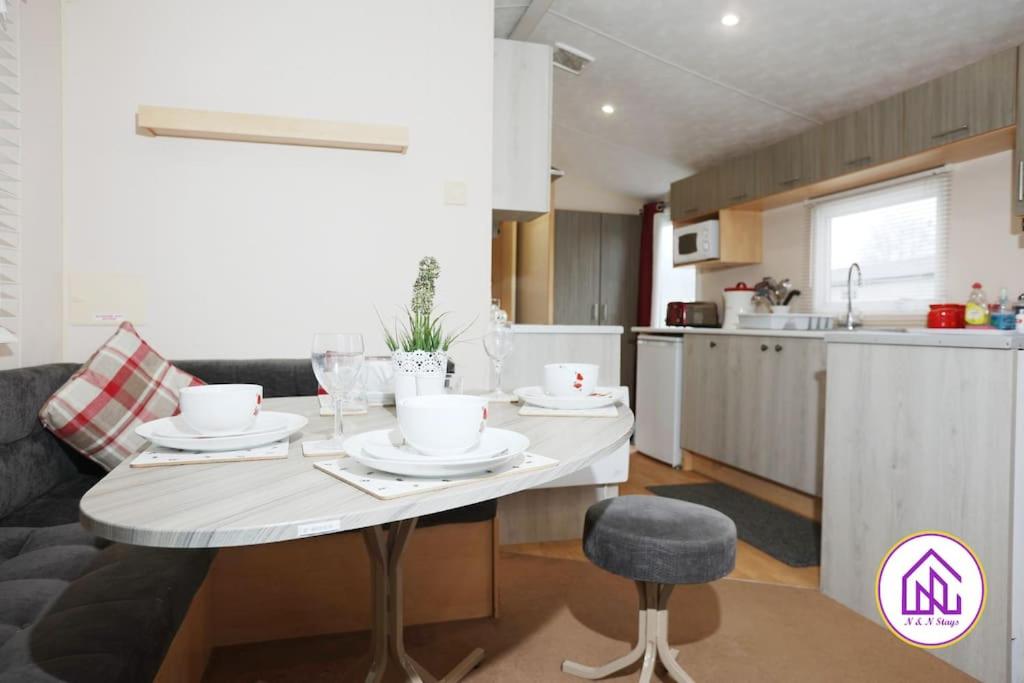 a kitchen with a table with dishes on it at Bumble Bee Lodge, Hoburne Cotswold Holiday Park in South Cerney
