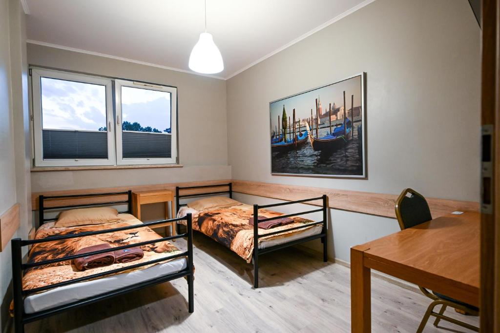 two beds in a room with a table and two windows at Hostel CENTRUM in Radom